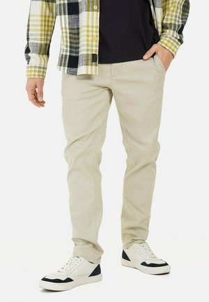 Beige slim-fit pants, cotton fabric, paired with a plaid flannel shirt in yellow and black, and white sneakers with navy accents.