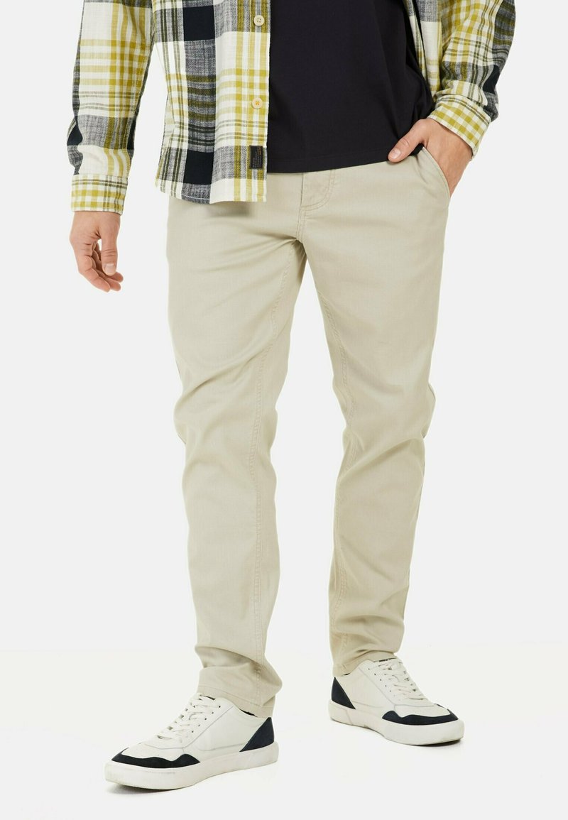 Beige slanke bukser i bomuldsstof, parret med en ternet flannel skjorte i gul og sort, samt hvide sneakers med marineblå accenter.