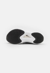 Semelle de chaussure de sport en noir et blanc avec une surface en caoutchouc texturé, une découpe dans la semelle intermédiaire et un logo de marque visible. Forme arrondie avec des rainures.