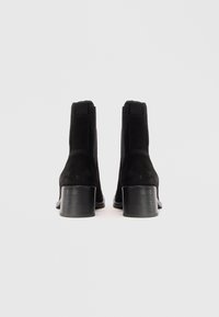 Stivaletti neri in suede fino alla caviglia con tacco a blocco medio, pannelli laterali elastici e un finish liscio. Design semplice senza hardware visibile.