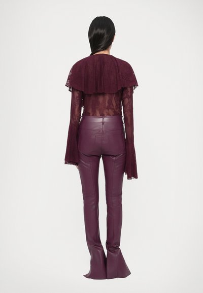 Bordó csipkefelső fodros gallérral, hozzá illő, magas derekú, testhez simuló bőrnadrággal, amelynek szárai szétflarelt kivitelűek.