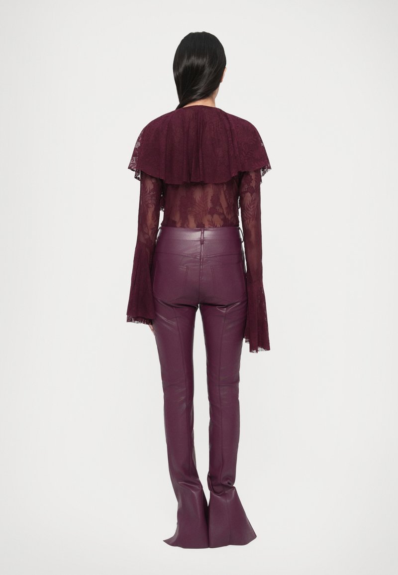 Dieprode kanten top met een gerufflede kraag, gecombineerd met hooggetailleerde, aansluitende leren broek in bijpassend dieprood, met uitlopende pijpen.
