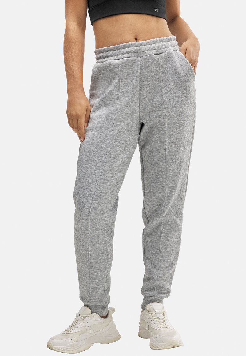 Pantalones de chándal grises con un corte ajustado, cinturilla elástica, bolsillos laterales y costuras en contraste. Combinados con zapatillas blancas.
