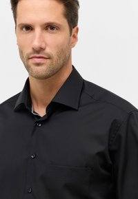 Camicia nera a maniche lunghe realizzata in tessuto morbido, con colletto classico, taschino sul petto e un motivo contrastante delicato all'interno del colletto.