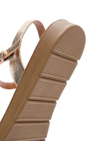 Sandali con cinturino metallico dorato, suola in gomma color marrone con texture e linee orizzontali sollevate. Il tacco offre un leggero rialzo per il comfort.
