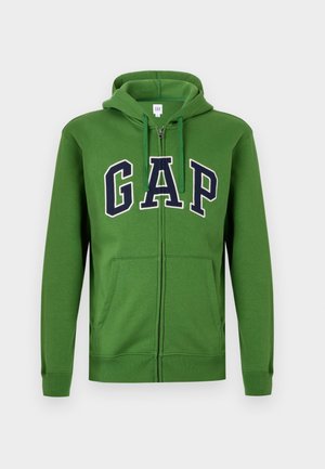 Grüne Kapuzenjacke mit Reißverschluss und frontalen Taschen, mit "GAP" in fetten marineblauen Buchstaben. Gefertigt aus weichem Stoff mit glatter Textur und verstellbarem Kapuzenbereich.