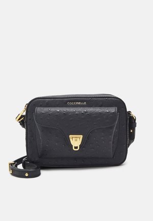 Zwarte, gestructureerde lederen crossbodytas met gouden voorvaksluiting en verstelbare riem, met "COCCINELLE"-logo boven het vakje.