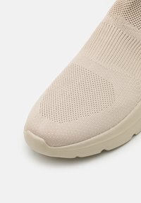 Beige strikket sneaker med en teksturert mesh-overdel, rund tå og gummisåle. Har en elastisk mansjett for enkel påkledning.