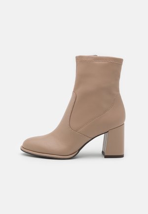Beige ankelstøvle med rund tå, sidelås og blokhæl med metallisk detalje, vist på hvid baggrund.