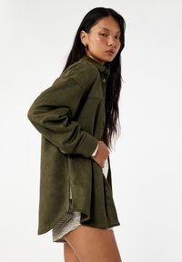 Olivgrüne Button-Up-Hemjacke aus weichem, wildlederähnlichem Material. Sie hat einen lässigen Schnitt, Seitenschlitze und leicht oversized Ärmel.