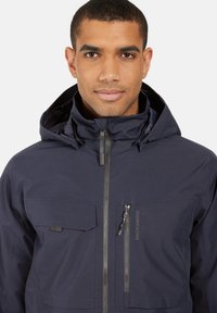 Meripainted kestävä takki vetoketjulla edessä, säädettävällä hupulla ja useilla taskuilla. Ominaisuuksiin kuuluu mattapintainen tekstuuri ja minimaalinen brändäys.