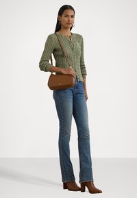 Cardigan vert en tricot torsadé, jeans droits bleus et bottines à talons brunes. Sac bandoulière marron avec un détail en logo doré.