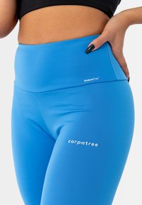 Leggings blu ad alta vita realizzati in materiale elastico. Presentano una texture liscia e loghi bianchi: "EnduraFlex" e "carpatree."