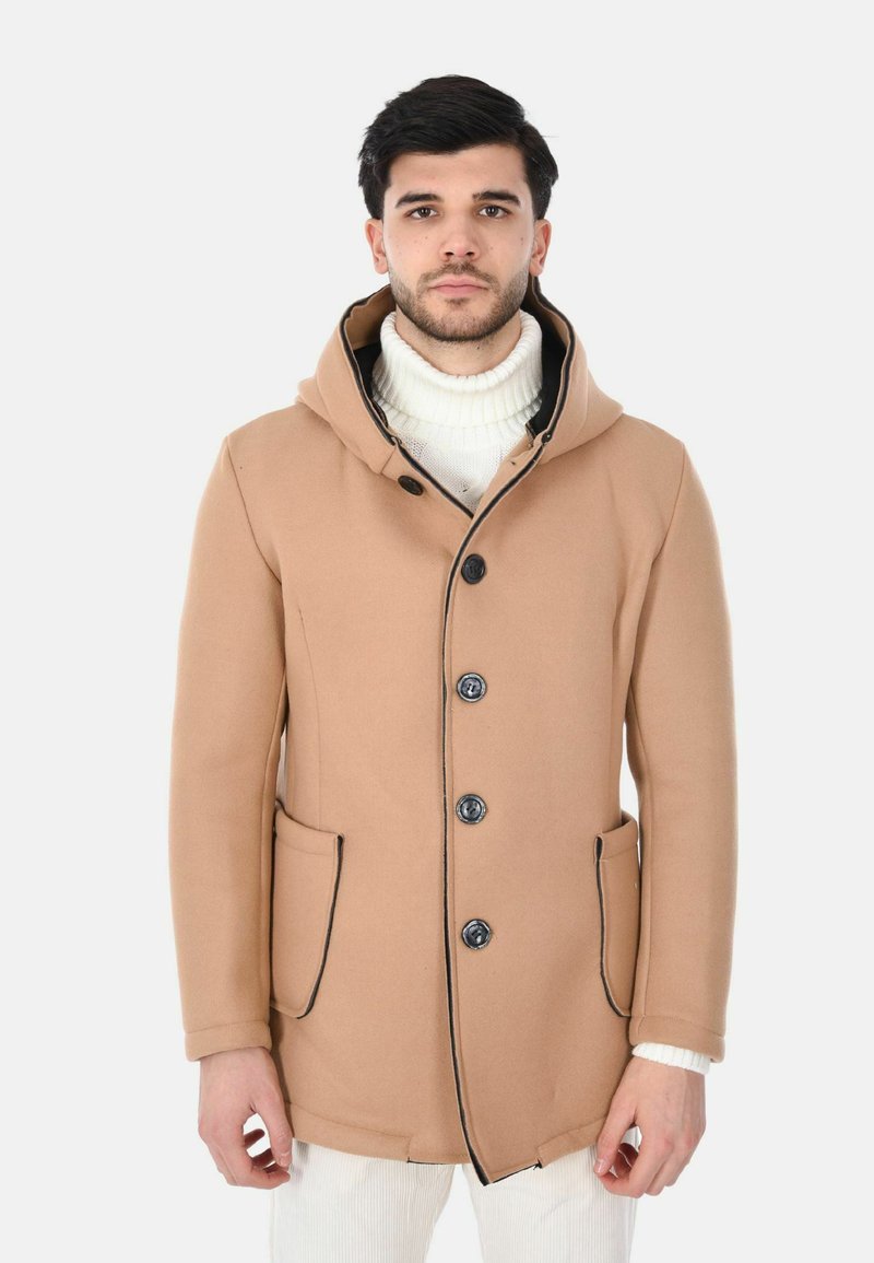 Cappotto con cappuccio marrone con rifiniture nere, caratterizzato da cinque bottoni, due tasche laterali e una texture morbida, indossato sopra un maglione bianco.
