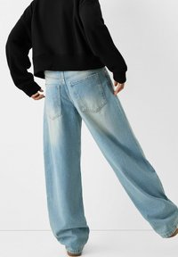 Jeans de tiro alto de mezclilla color azul claro y de pierna ancha. Presentan un patrón desgastado, dos bolsillos traseros y un ajustado relajado. Combinados con un suéter negro corto.