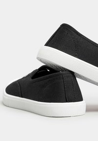 Scarpe nere in tela con profilo basso, suole in gomma bianca e design minimalista. Presentano dettagli cuciti e pannelli laterali elasticizzati.
