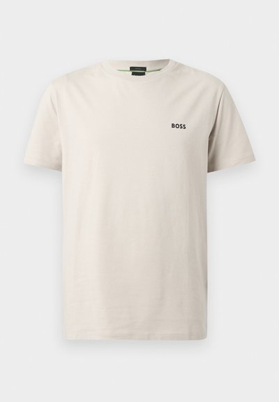 T-shirt en coton beige clair avec col rond, manches courtes et un petit logo noir "BOSS" sur la poitrine gauche. Texture lisse.