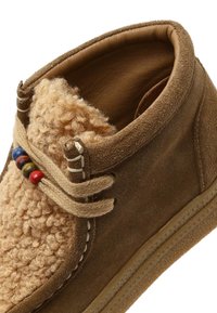 Brązowe zamszowe botki sięgające do kostki z teksturowanym, tanowym wełnianym wierzchem, beżowymi sznurowadłami i kolorowymi drewnianymi koralikami po boku. Gumowa podeszwa.