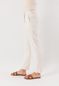 Pantaloni color crema con una vestibilità rilassata, fronte plissettato e vita elasticizzata. Abbinati a sandali marroni con dettagli a intaglio.