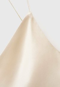 Camisole en satin de couleur beige clair avec des bretelles fines, présentant une texture lisse et brillante ainsi qu'un design triangulaire.