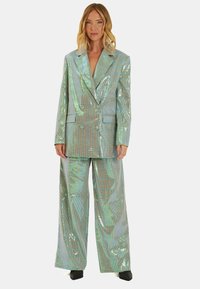 Iridescent tweed-pak bestaande uit een dubbelzijdig colbert met brede revers en baggy broek, beiden met een geruit patroon en glanzende afwerking.