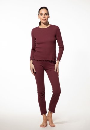 Maroone langslijfsblouse en fitted broek gemaakt van zachte stof met ruches aan de onderkant en minimale naden, ontworpen voor comfort en bewegingsvrijheid.