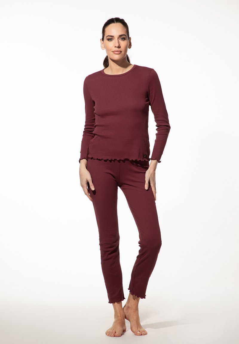 Maroone langslijfsblouse en fitted broek gemaakt van zachte stof met ruches aan de onderkant en minimale naden, ontworpen voor comfort en bewegingsvrijheid.