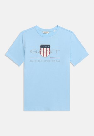 Ανοιχτό μπλε κοντομάνικο μπλουζάκι με το λογότυπο "GANT", κόκκινο και λευκό έμβλημα ασπίδας με το "1949" και το κείμενο "American Sportswear" μπροστά.
