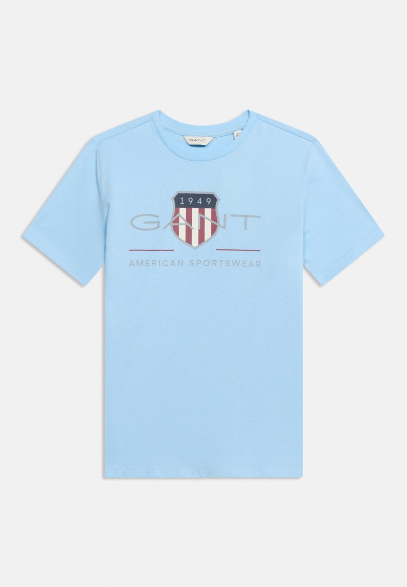 Ανοιχτό μπλε κοντομάνικο μπλουζάκι με το λογότυπο "GANT", κόκκινο και λευκό έμβλημα ασπίδας με το "1949" και το κείμενο "American Sportswear" μπροστά.