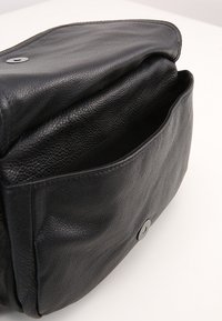 Svart läderväska med en strukturerad yta, stor huvudfack och knäppning med knapp. Har en mjuk och flexibel design.