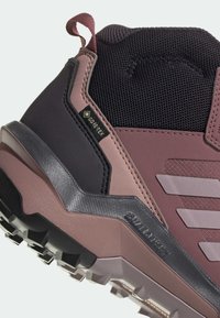 GORE-TEX felirattal ellátott lábbeli, fekete és mályva anyagok keverékével, texturált kiegészítőkkel és egyenetlen talppal, amelynek kiemelkedő barázdái vannak.