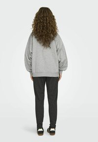 Šedý oversized svetr s nadýchanými rukávy, kombinovaný s černými strukturovanými kalhotami. Má pohodlný střih a žebrované manžety. Obuví jsou černobílé tenisky.