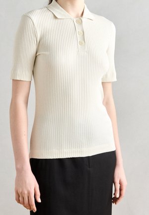 Kremowa koszulka polo z krótkim rękawem, wykonana z prążkowanego dzianiny z miękkim kołnierzem. Posiada trzy guziki z przodu oraz dopasowany krój.