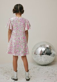 Sidabrinė blizgučiais suknelė su rožinių gėlių raštais, trumpomis ruffle rankovėmis, su išpjova nugaroje, derinama su metaliniais sidabriniais kaubojiškais batais.