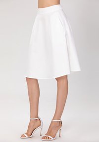 Jupe A-line blanche en tissu de coton avec une texture lisse, dotée de poches latérales et d'une taille haute. Accompagnée de talons hauts blancs.