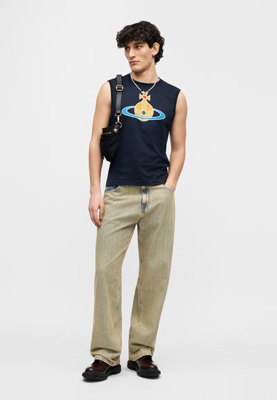 Μπλε ναυτικό αμάνικο μπλουζάκι με πολύχρωμο γραφικό, συνδυασμένο με ανοιχτόχρωμο ριγέ παντελόνι με φαρδιά μπατζάκια και σκουρόχρωμα χοντρά μποτάκια. Αξεσουάρ: μικρή μαύρη τσάντα.