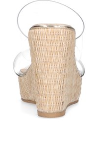Sandalia de cuña con parte superior de paja tejida natural, correa de tobillo transparente y suela de tono beige claro. Presenta un detalle metálico cerca de la parte superior.