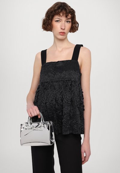 Top negru cu textură florală, cu decolteu pătrat și bretele late, asortat cu o geantă metalică argintie și pantaloni negri.