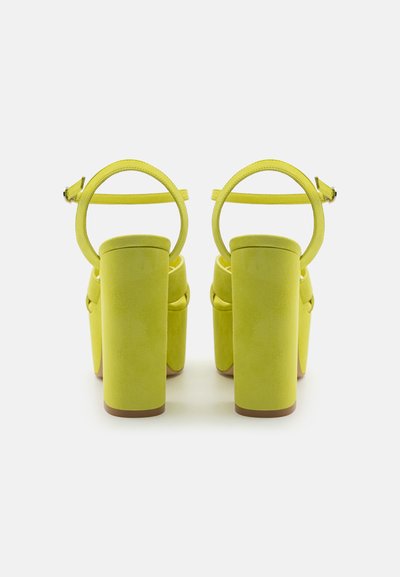 Sandales à talons hauts en daim jaune avec un épais talon bloc, un design à double sangle et une boucle au niveau de la cheville pour un maintien sécurisé. Surface texturée.