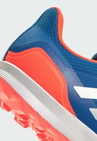 Blå sportskor med orange detaljer, strukturerat material och vit logotyp. Har en kontrasterande gummisula med mönstrat grepp.