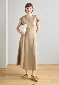 Brown, ankle-length dress with short sleeves, subtle texture, and a fitted bodice. Paired with beige slip-on shoes and a white clutch.