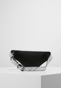Svart och vit Calvin Klein midjeväska med en slät yta, försedd med ett brett rem som har tryckt logotyp och en dragkedja i huvudfacket.