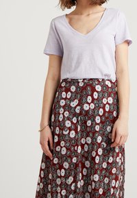 Ljuslila t-shirt med v-ringning i kombination med en lång bordeauxfärgad kjol med ett blommönster i vitt och svart. Slät tygtextur.