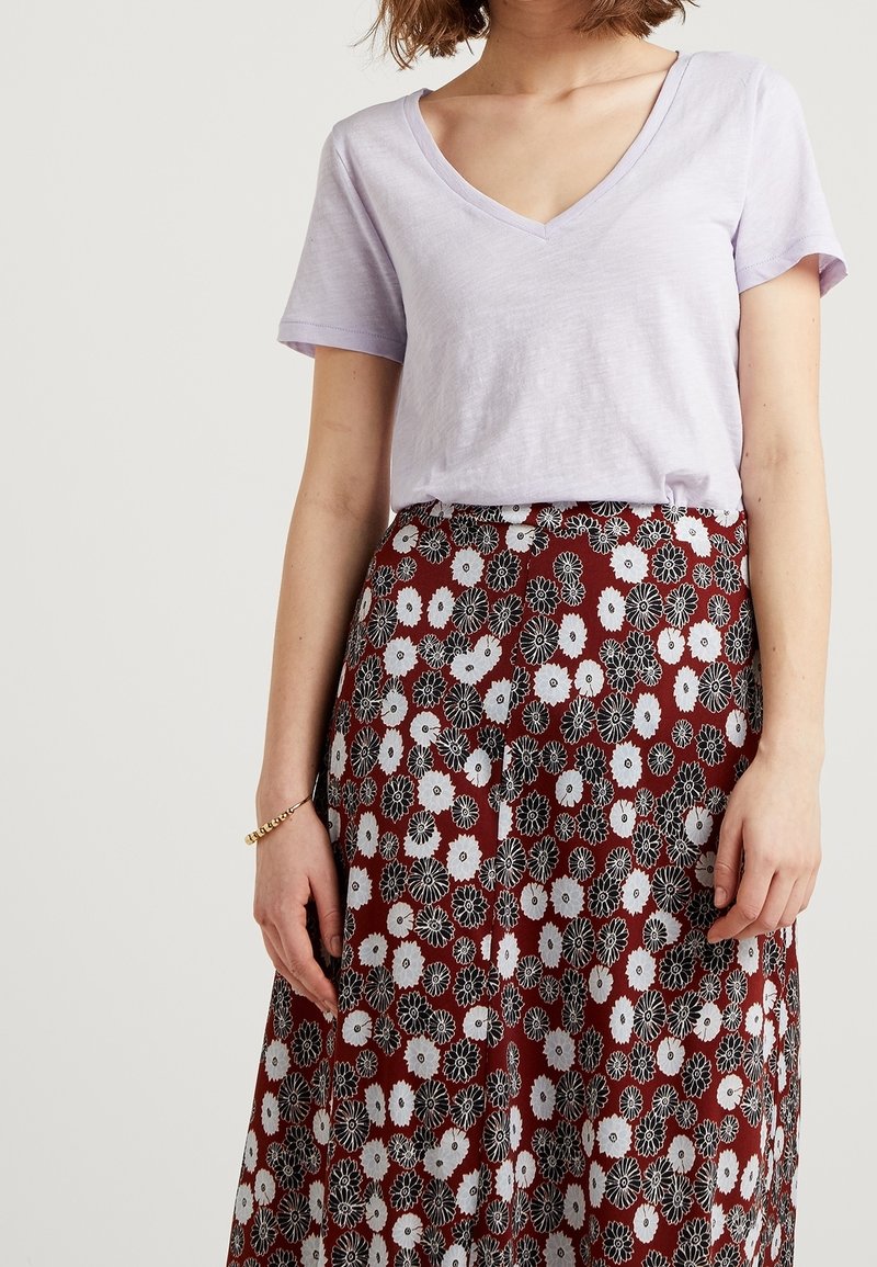 Ljuslila t-shirt med v-ringning i kombination med en lång bordeauxfärgad kjol med ett blommönster i vitt och svart. Slät tygtextur.