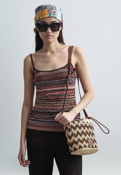 Ριγωτό πλεκτό αμάνικο τοπάκι σε κόκκινο, πορτοκαλί και καφέ χρώμα; παντελόνι με μαύρο ζιγκ-ζαγκ σχέδιο; υφαντή τσάντα από ψάθα με καφέ δερμάτινες λεπτομέρειες και κορδόνι.