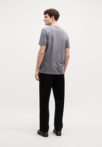 Grijze t-shirt met korte mouwen en een ronde hals, gecombineerd met zwarte broek. De stof lijkt glad en aangesloten met een strakke silhouette.