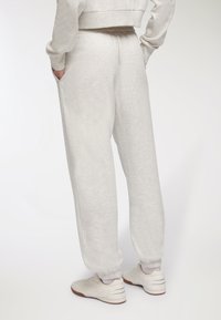 Jasnoszare dresy z elastycznym pasem i mankietami, z bocznymi kieszeniami i miękkim, teksturowanym materiałem. Noszone z jasnymi sneakersami.