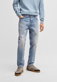 Vaqueros de mezclilla de un azul claro con un corte relajado, que presentan áreas desgastadas y desvanecidas. Combinados con zapatillas en tonos marrón y negro y un sudadera azul claro.