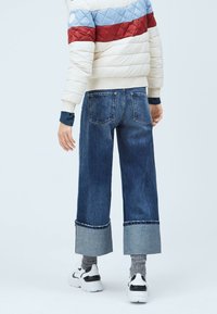 Džíny z denimu se širokým, zkráceným střihem nohavic, s kontrastní manžetou z jiného materiálu. Kombinovány s prošívanou péřovou bundou v krémové, modré a červené barvě.