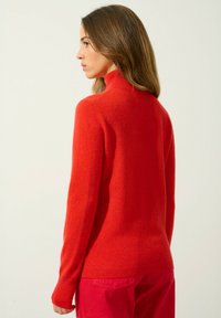 Maglione a collo alto rosso in maglia con maniche lunghe, polsini a coste e una texture morbida, abbinato a pantaloni rosa dal fit casual.